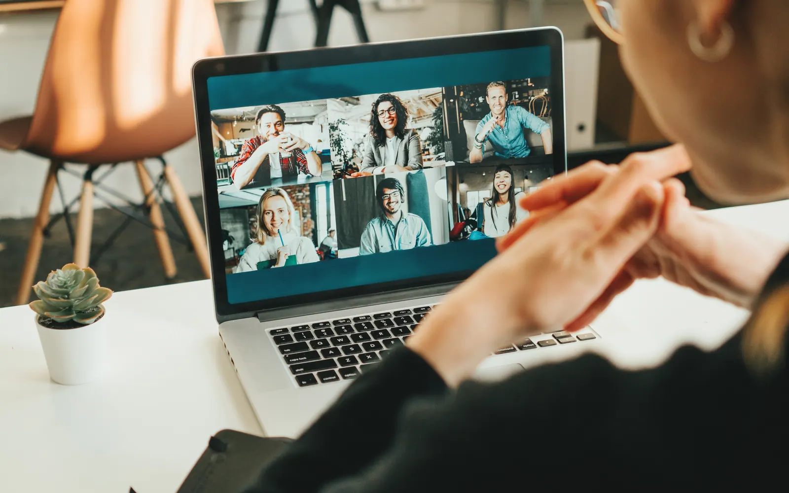 Iemand volgt een videovergadering op de laptop, met de deelnemers in beeld